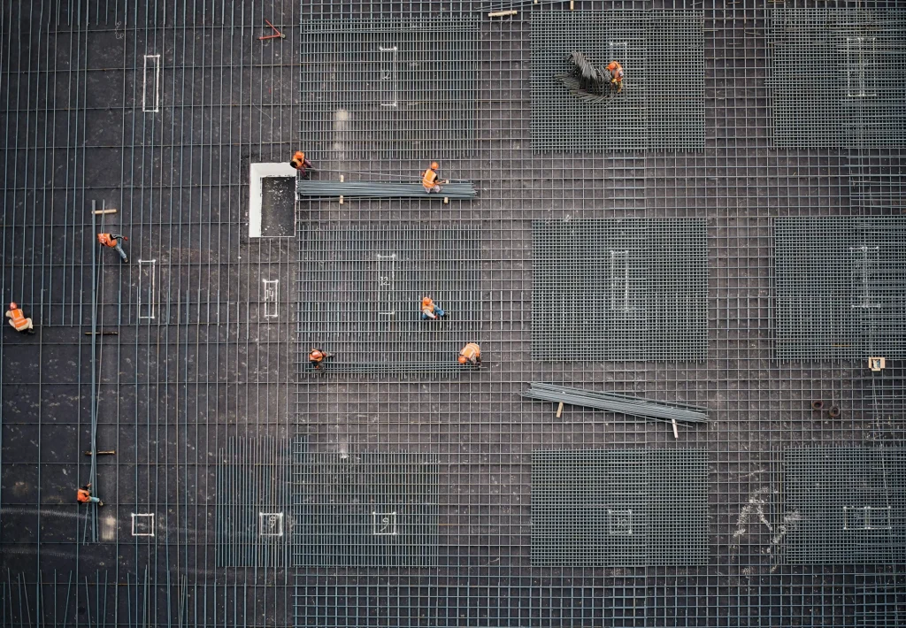 Operai al lavoro su armature in acciaio per fondazioni in cantiere edile, vista dall’alto